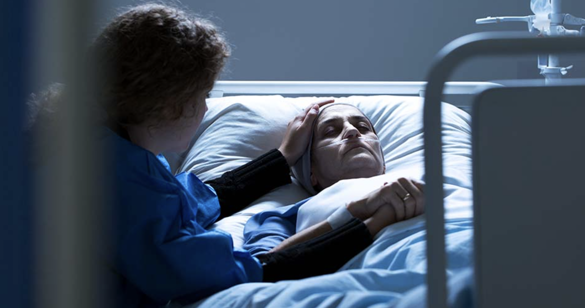 A patient lying in bed with their loved one next to them, caressing their hair.